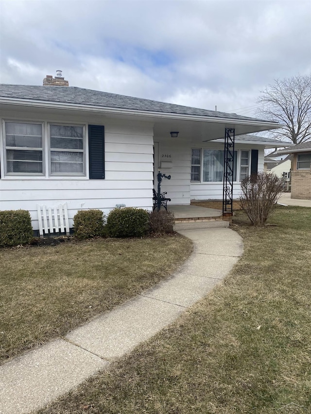 view of front of home featuring covered porch, a front lawn, and roof with shingles