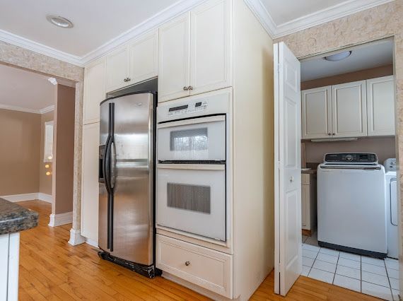 kitchen with double oven, white cabinetry, light wood-style floors, ornamental molding, and stainless steel fridge with ice dispenser