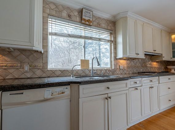 kitchen featuring white dishwasher, under cabinet range hood, a sink, gas stovetop, and ornamental molding