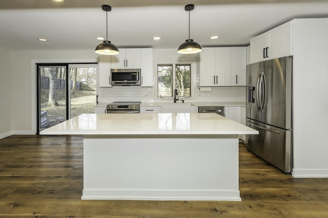 kitchen with appliances with stainless steel finishes, decorative light fixtures, a kitchen island, and white cabinets