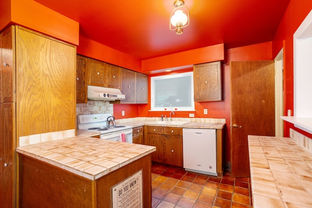 kitchen featuring tile countertops, sink, backsplash, kitchen peninsula, and white appliances