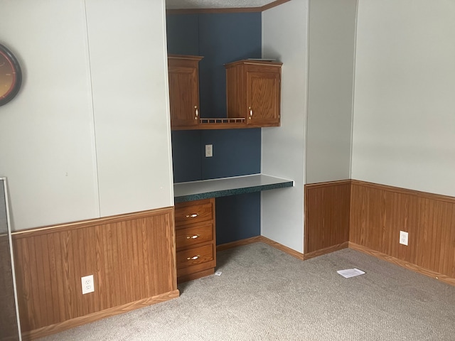 unfurnished office featuring light colored carpet, a wainscoted wall, wood walls, visible vents, and built in desk