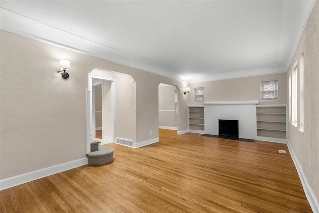 unfurnished living room with a brick fireplace, hardwood / wood-style flooring, and crown molding