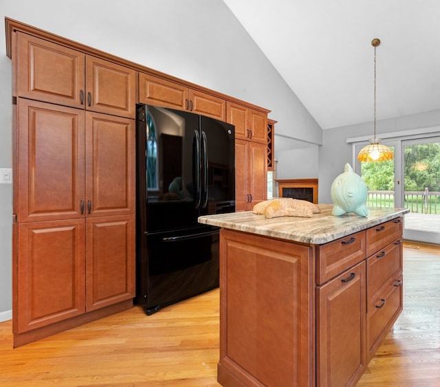 kitchen featuring a kitchen island, black refrigerator, hanging light fixtures, light hardwood / wood-style floors, and light stone countertops