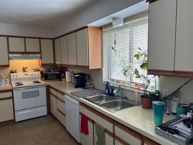 kitchen with tile patterned floors, under cabinet range hood, a sink, white appliances, and light countertops