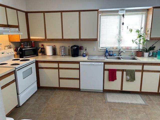 kitchen with a sink, white appliances, under cabinet range hood, and light countertops