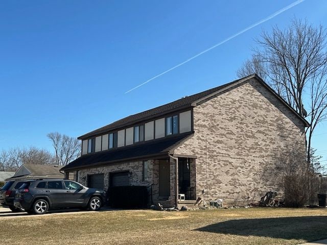 exterior space featuring brick siding, an attached garage, and a lawn