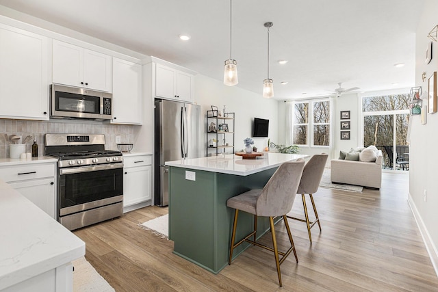 kitchen with a kitchen island, decorative light fixtures, tasteful backsplash, white cabinets, and stainless steel appliances