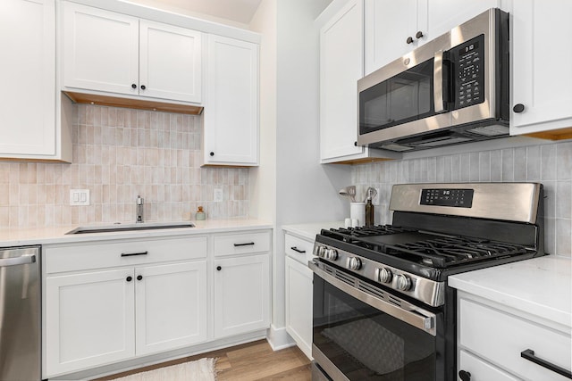 kitchen featuring sink, white cabinetry, stainless steel appliances, light hardwood / wood-style floors, and decorative backsplash