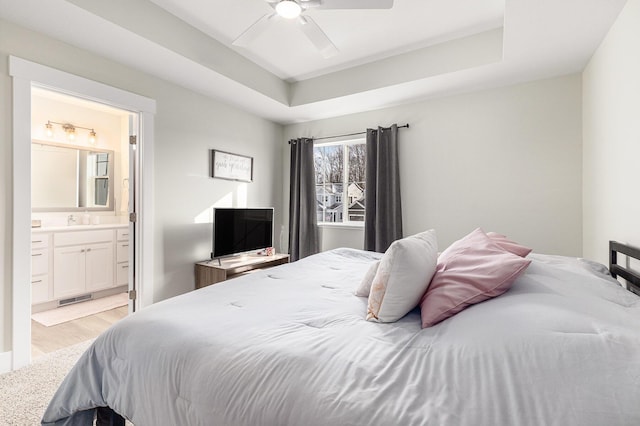 bedroom with sink, ensuite bath, ceiling fan, a raised ceiling, and light wood-type flooring