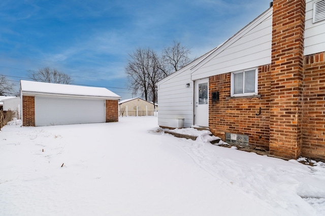 snowy yard with a garage and an outbuilding