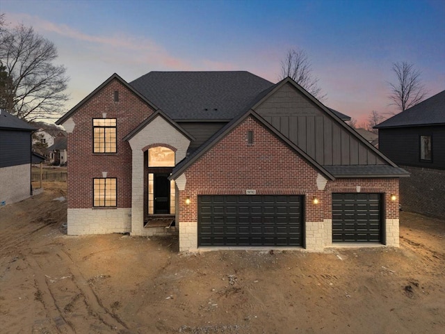 view of front of property featuring driveway, roof with shingles, an attached garage, board and batten siding, and brick siding