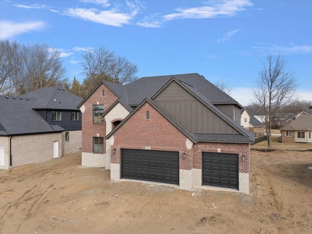 view of front of home featuring brick siding, roof with shingles, dirt driveway, an attached garage, and board and batten siding