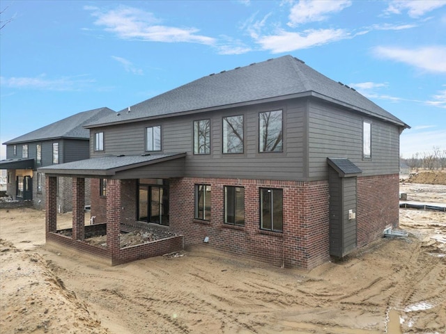 back of house with a garden, roof with shingles, and brick siding