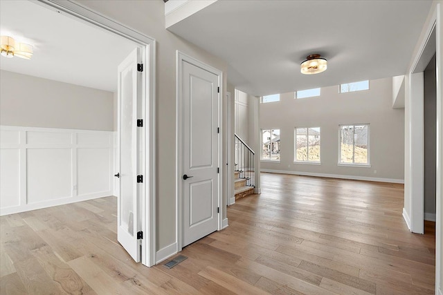 hall featuring light wood-style flooring, visible vents, a decorative wall, and stairway