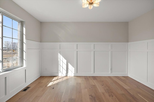 unfurnished room with a healthy amount of sunlight, light wood finished floors, visible vents, and a decorative wall