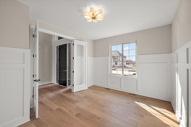 spare room with a wainscoted wall, light wood-type flooring, and visible vents