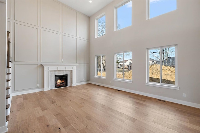 unfurnished living room with baseboards, a tiled fireplace, visible vents, and light wood-style floors