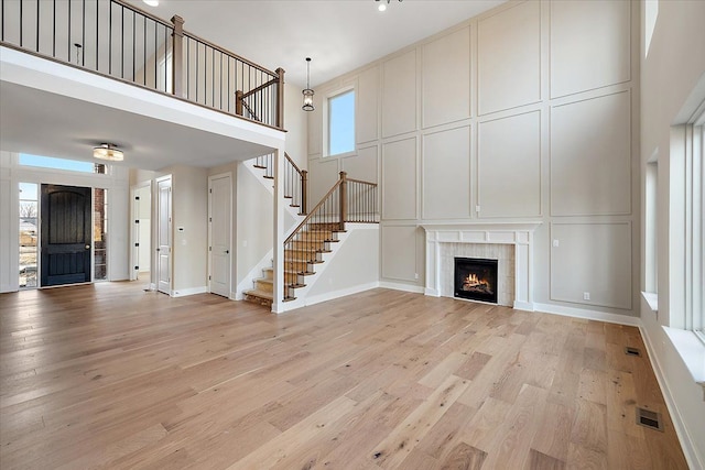 unfurnished living room featuring visible vents, a towering ceiling, stairs, light wood-style floors, and a decorative wall