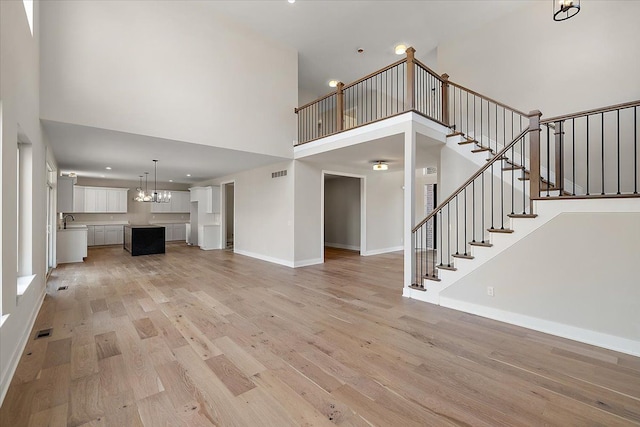 unfurnished living room featuring light wood finished floors, stairs, baseboards, and a sink