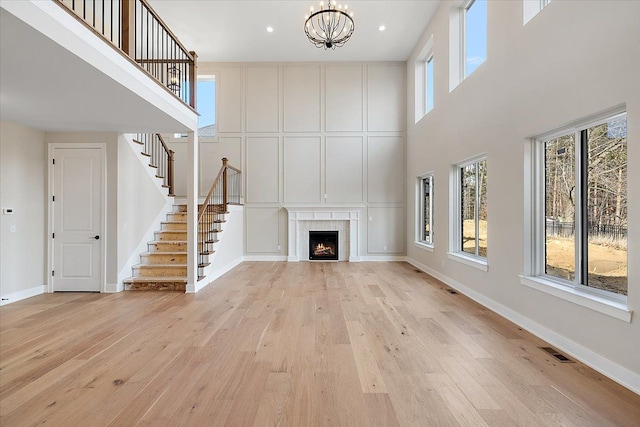 unfurnished living room with stairway, a tiled fireplace, an inviting chandelier, light wood-style floors, and baseboards