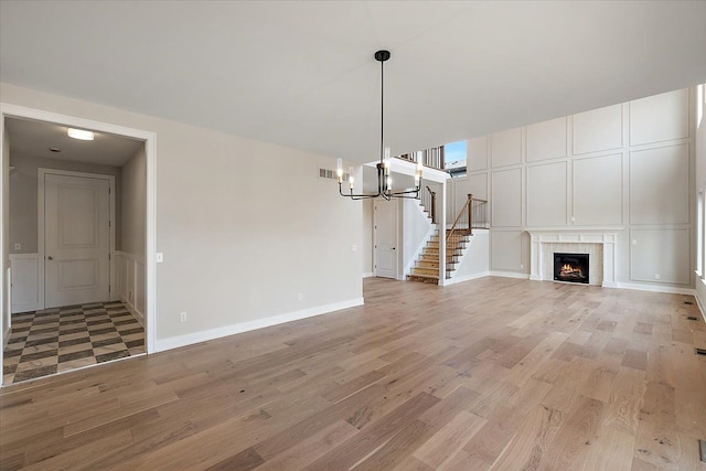 unfurnished living room featuring a fireplace, a decorative wall, light wood finished floors, and stairs