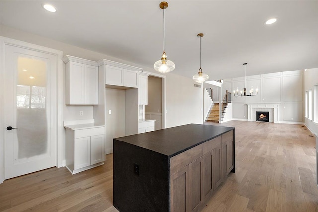 kitchen with a center island, white cabinets, light wood finished floors, and a premium fireplace