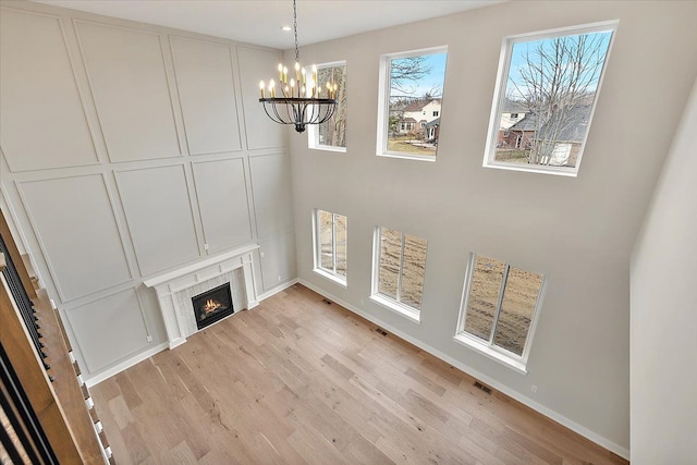 unfurnished living room with a notable chandelier, a fireplace, a decorative wall, and light wood finished floors