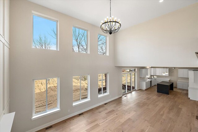 unfurnished living room featuring a chandelier, a high ceiling, visible vents, and light wood-style floors