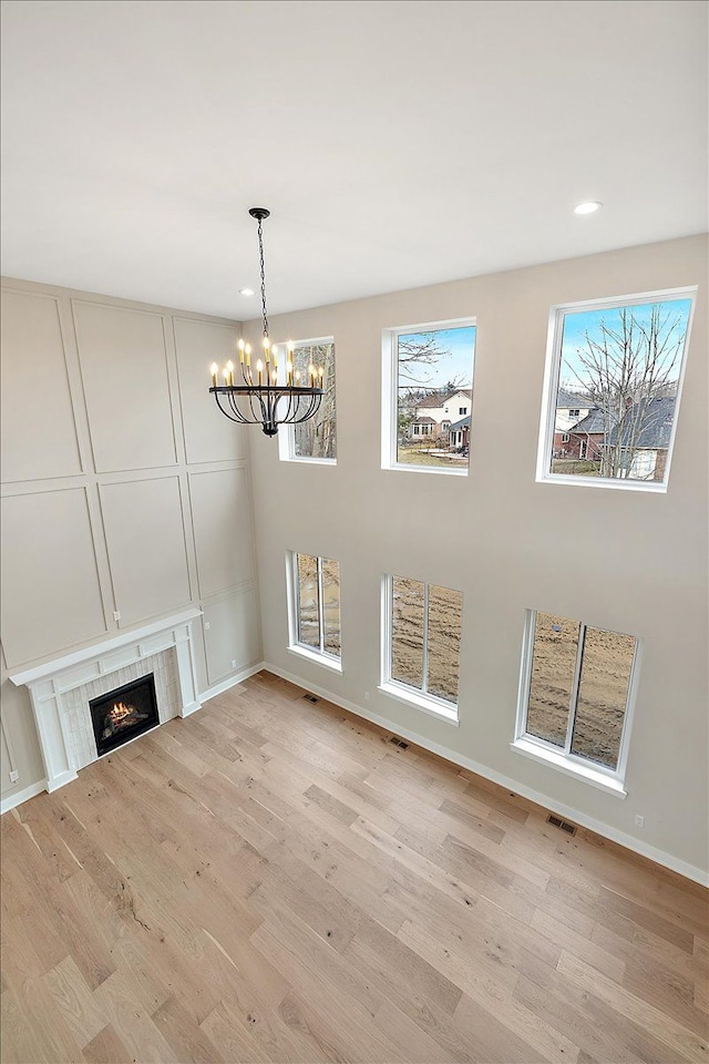 unfurnished living room featuring light wood-style floors, an inviting chandelier, a tile fireplace, and a healthy amount of sunlight