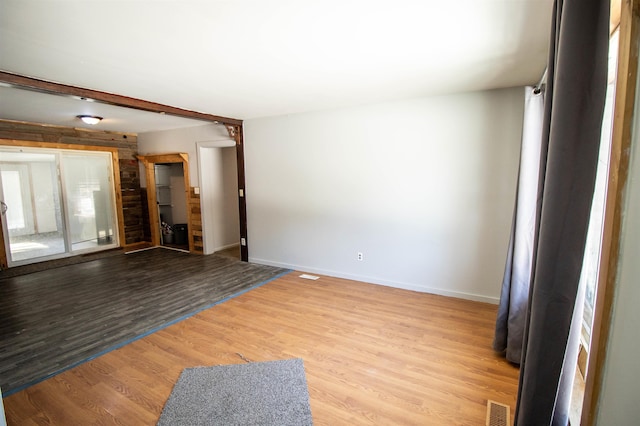 spare room with beamed ceiling and light wood-type flooring