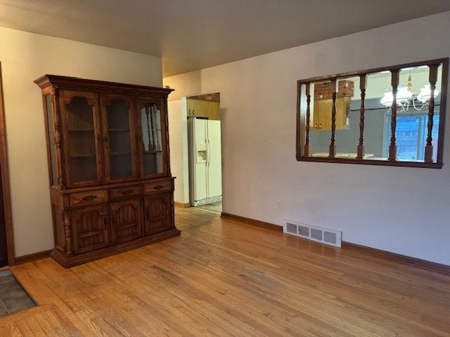 empty room featuring an inviting chandelier and light hardwood / wood-style floors