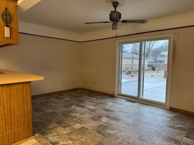 empty room featuring ceiling fan and wooden walls