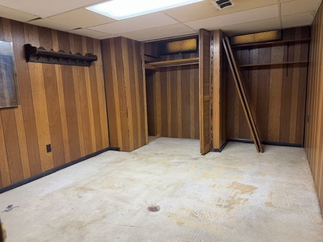 basement featuring a drop ceiling and wooden walls