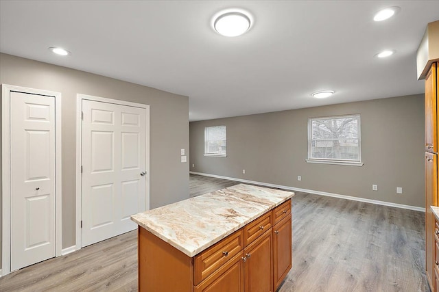 kitchen with light stone countertops, a kitchen island, and light hardwood / wood-style flooring