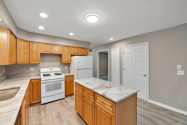 kitchen with a kitchen island, sink, light stone counters, white appliances, and light hardwood / wood-style flooring