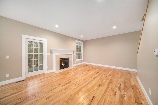 unfurnished living room featuring a wealth of natural light, a tile fireplace, and light wood-type flooring