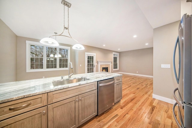 kitchen with sink, decorative light fixtures, stainless steel appliances, light stone countertops, and light hardwood / wood-style floors