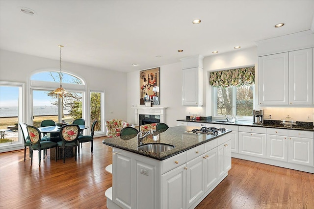 kitchen featuring dark stone countertops, an island with sink, white cabinetry, and sink