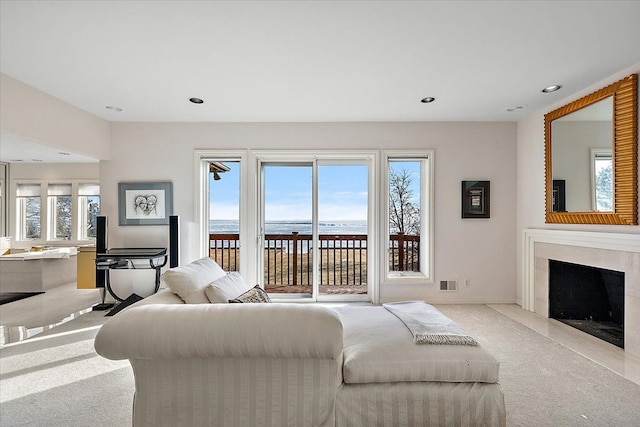 living room featuring light carpet, a water view, and a high end fireplace