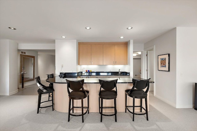 kitchen with a kitchen bar, light carpet, kitchen peninsula, and light brown cabinets