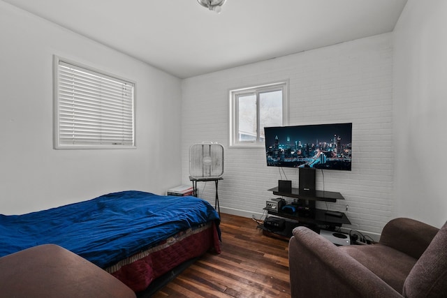 bedroom with dark hardwood / wood-style floors and brick wall