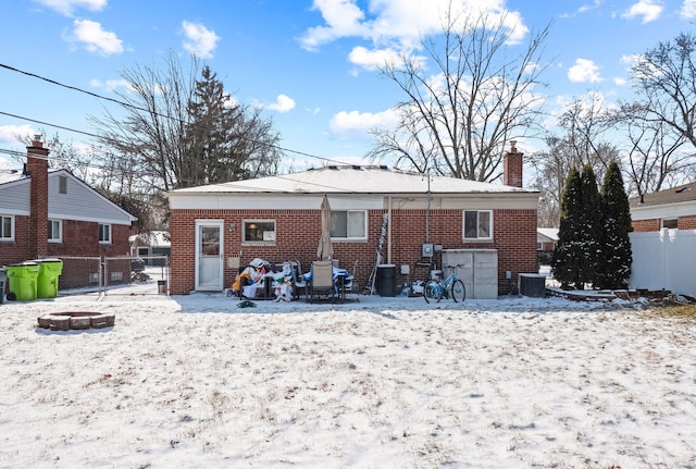 snow covered rear of property with a fire pit and central AC