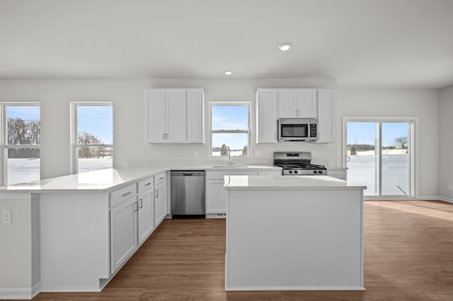 kitchen with a peninsula, appliances with stainless steel finishes, white cabinets, and a sink