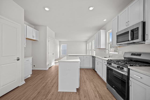 kitchen featuring appliances with stainless steel finishes, white cabinetry, a sink, and light wood finished floors