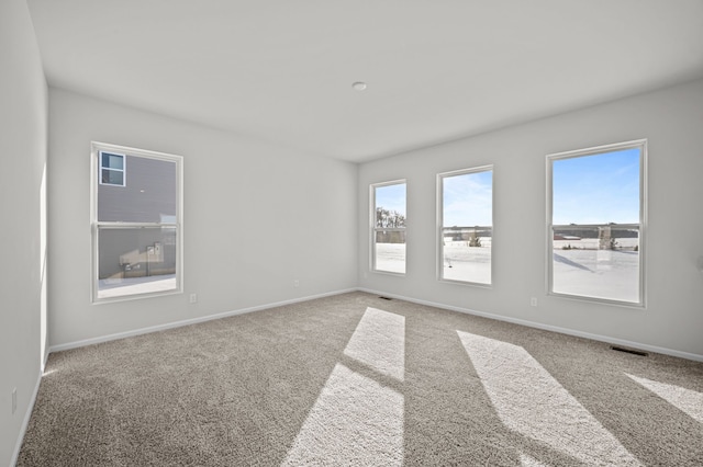 spare room featuring carpet floors, a wealth of natural light, visible vents, and baseboards