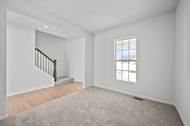 carpeted empty room with stairway, baseboards, and visible vents