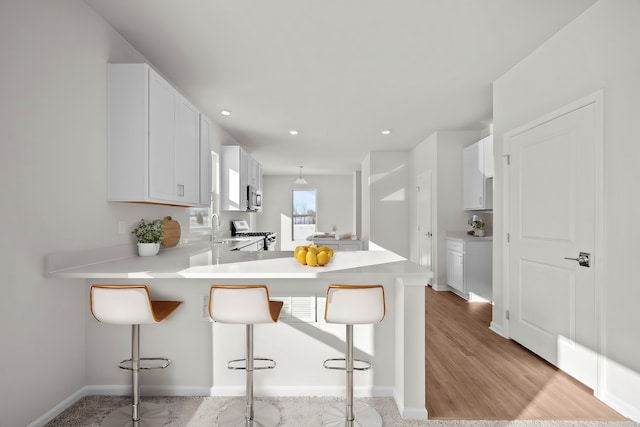 kitchen with a peninsula, a sink, a kitchen breakfast bar, light countertops, and appliances with stainless steel finishes