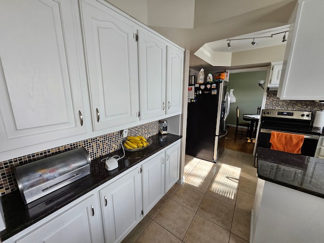 kitchen featuring white cabinetry, dark stone countertops, light tile patterned floors, stainless steel appliances, and backsplash