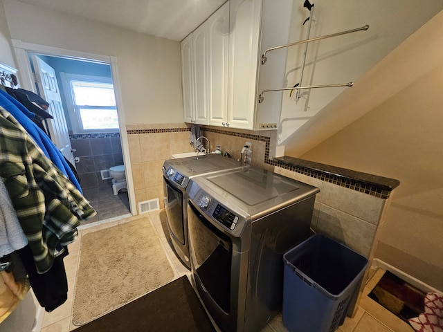 washroom with cabinets, tile walls, washing machine and clothes dryer, and light tile patterned floors